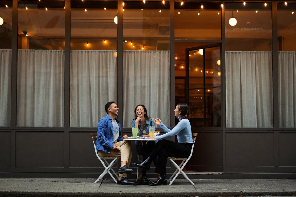 Drie mensen aan een tafeltje bij een buitencafé in de avond, warme lichtjes, ontspannen sfeer