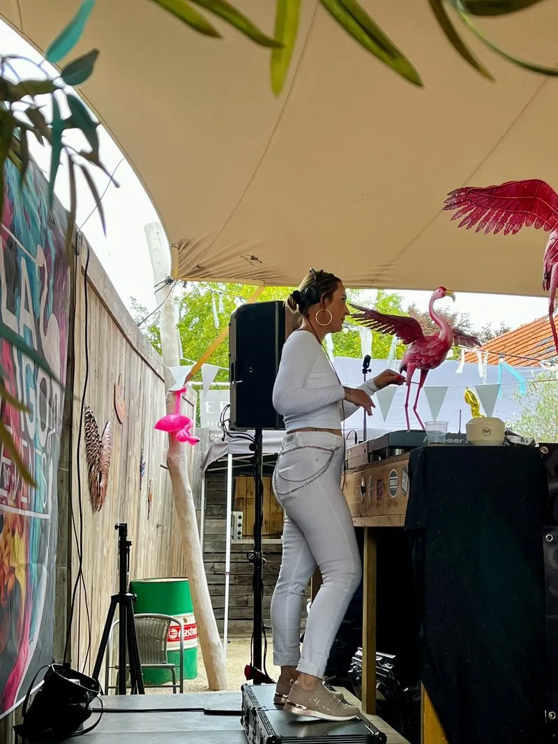 DJ Gina achter de draaitafels bij Flamigo, met een flamingo-decoratie op de achtergrond