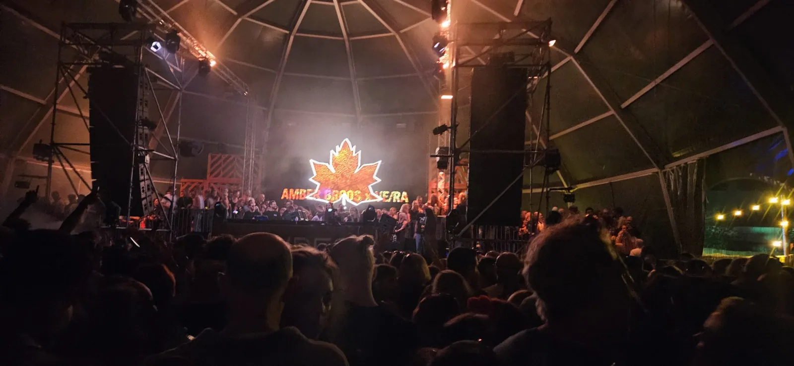 Dj-booth in een tent met een oplichtend esdoornblad op het scherm, gezien vanaf de dansvloer