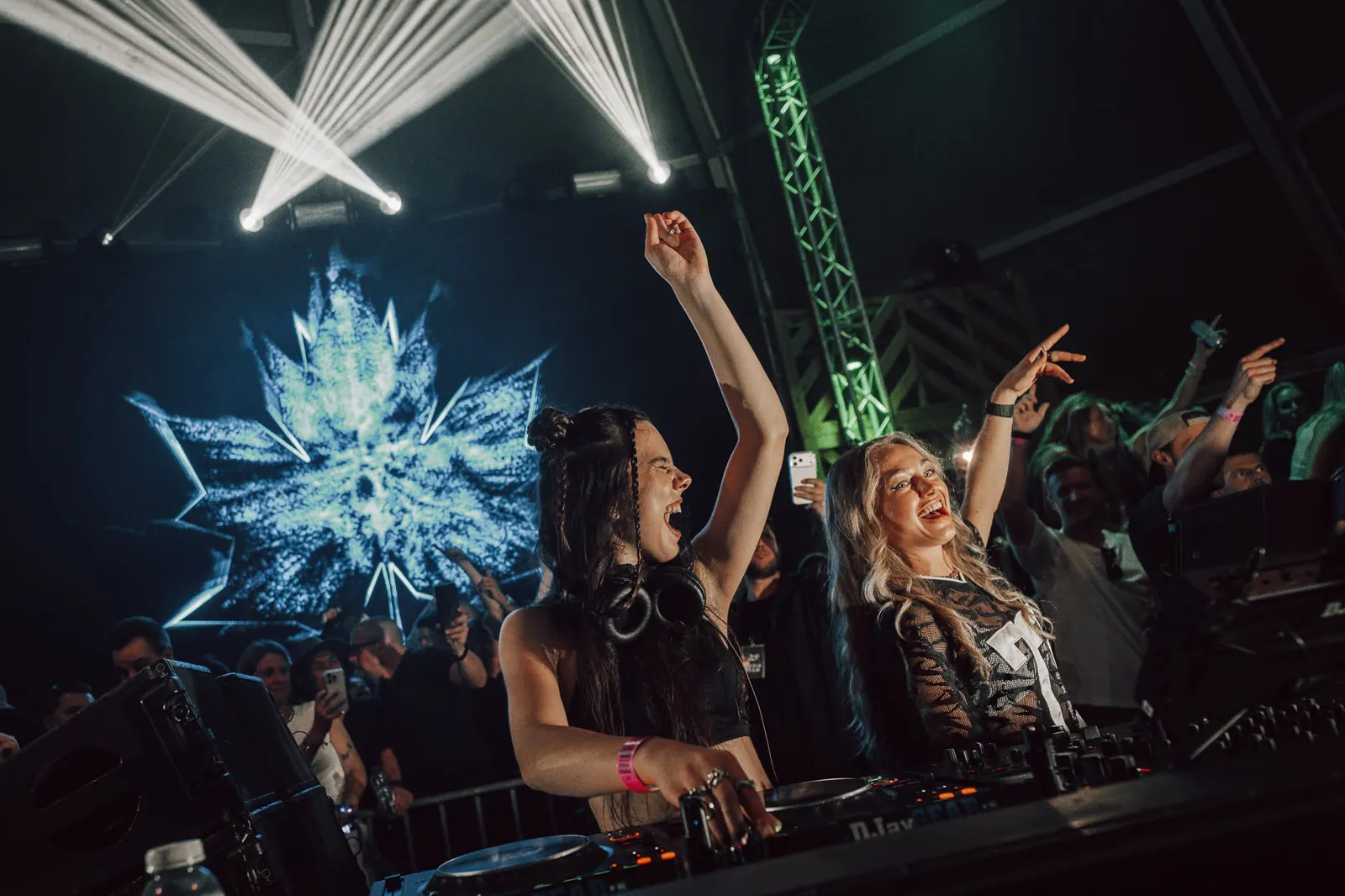 Twee dj&rsquo;s achter de draaitafels, een van hen met opgestoken arm, voor een scherm met een esdoornblad en lichtstralen