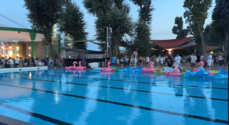 Buitenzwembad bij avondschemering met roze en blauwe opblaasflamingo&rsquo;s op het water en bezoekers langs de rand