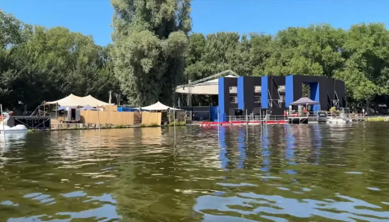 Uitzicht over het water op een podium en tenten aan de oever, omringd door bomen