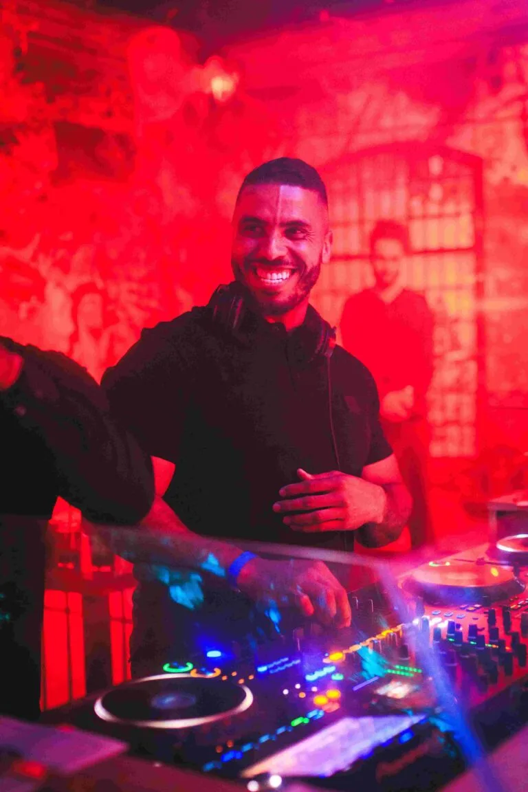 Een lachende dj achter de draaitafels, gehuld in rood licht, tijdens een Pineapple Club-avond.